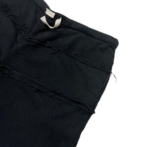 Puede incluir: Primer plano de un pantal&oacute;n de ch&aacute;ndal negro con detalles desgastados. El pantal&oacute;n tiene una cintura con cord&oacute;n y varias costuras horizontales desgastadas en la parte delantera. La tela parece ser un material suave y oscuro.