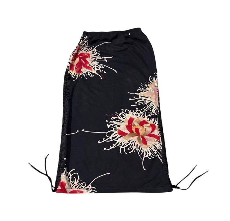 May include: Black drawstring skirt with a floral design. The skirt displays large, stylized flowers in shades of red, white, and pink. The flowers are set against a black background. The skirt has drawstrings at the waist and along the sides.