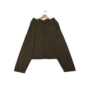 Puede incluir: Pantalones verde oliva con un diseño único de pernera ancha. Los pantalones tienen cierre de botón y cremallera, bolsillos delanteros y están colgados de una percha de madera. La tela parece ser de peso medio.