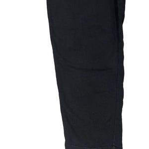 Puede incluir: Primer plano de un pantal&oacute;n negro. La tela es de un color oscuro y liso. El pantal&oacute;n tiene una pernera recta y un bajo con dobladillo. La imagen est&aacute; bien iluminada, destacando la textura y la forma de la prenda.