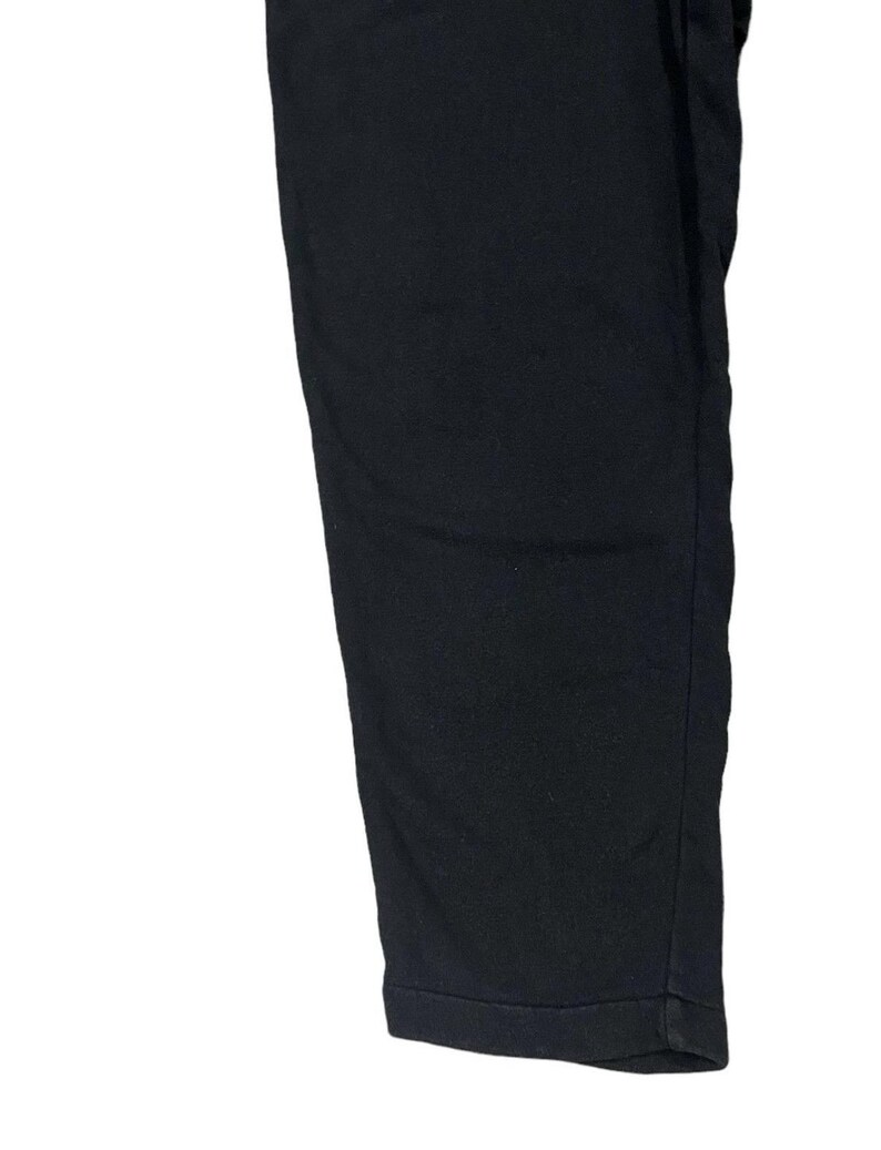 Puede incluir: Primer plano de un pantal&oacute;n negro. La tela es de un color oscuro y liso. El pantal&oacute;n tiene una pernera recta y un bajo con dobladillo. La imagen est&aacute; bien iluminada, destacando la textura y la forma de la prenda.