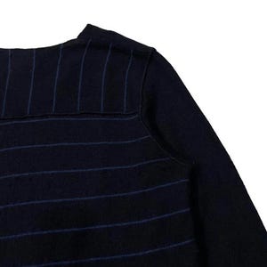 Puede incluir: Primer plano de un su&eacute;ter azul marino con finas rayas verticales de color azul claro. El su&eacute;ter tiene cuello redondo y mangas largas. La tela parece ser un material de punto suave.