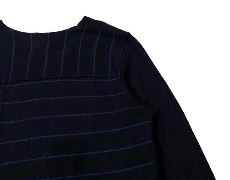 Puede incluir: Primer plano de un su&eacute;ter azul marino con finas rayas verticales de color azul claro. El su&eacute;ter tiene cuello redondo y mangas largas. La tela parece ser un material de punto suave.