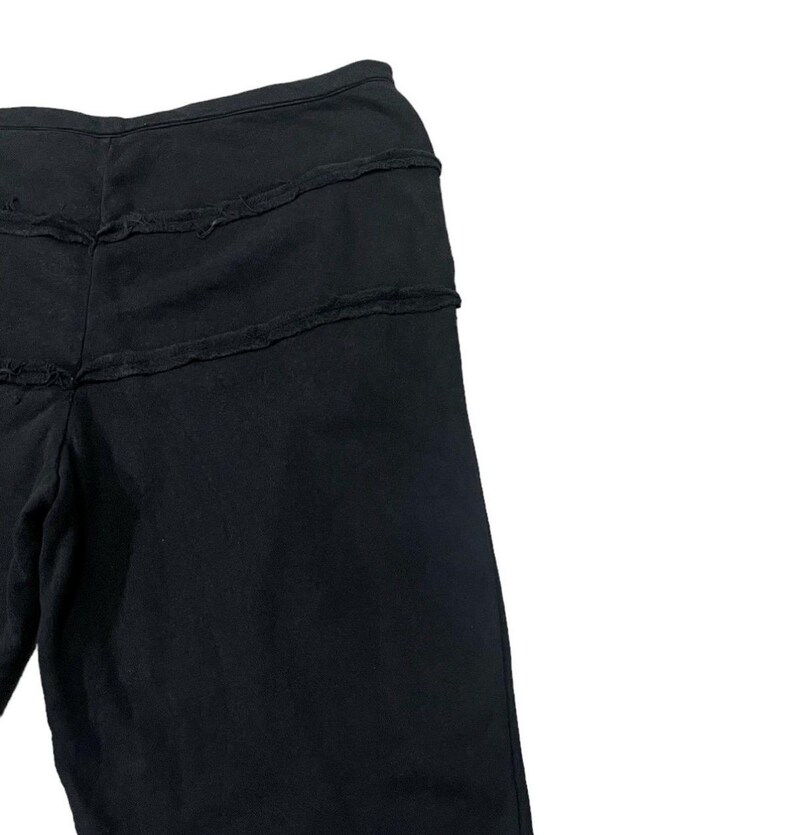 Puede incluir: Pantalones negros con tres costuras horizontales deshilachadas en la parte superior. Los pantalones parecen estar hechos de una tela oscura y suave. El dise&ntilde;o es sencillo e informal.