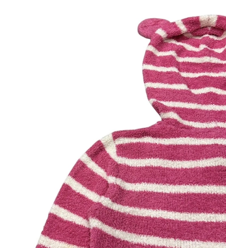 May include: A pink and white striped hooded sweater with a fuzzy texture. The hood features a small, rounded ear detail at the top. The sweater's stripes are horizontal and evenly spaced.