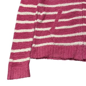 May include: Close-up of a pink and white striped sweater. The sweater has a soft, textured appearance and a horizontal stripe pattern. The sleeve and body are visible, showing the knit fabric.