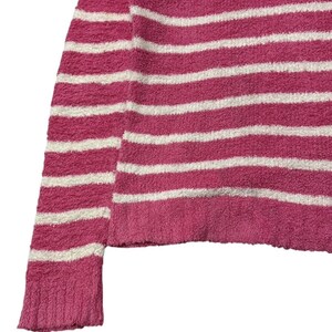 May include: Close-up of a pink and white striped sweater. The sweater has horizontal stripes and a textured, fuzzy appearance. The sleeve and hem are visible, showcasing the garment's construction and color scheme.