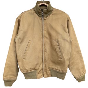 May include: A tan bomber jacket with a zip-up front, two front pockets, and a ribbed collar, cuffs, and hem. The jacket is hanging on a hanger. The collar, cuffs, and hem are olive green.