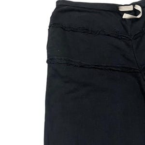 Puede incluir: Pantalones negros con detalles horizontales deshilachados. Los pantalones tienen cintura con cord&oacute;n y un ajuste relajado. La tela parece ser un material suave y oscuro, adecuado para ropa informal. El dise&ntilde;o presenta una est&eacute;tica &uacute;nica y desgastada.