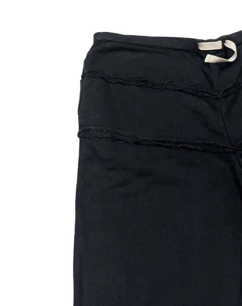Puede incluir: Pantalones negros con detalles horizontales deshilachados. Los pantalones tienen cintura con cord&oacute;n y un ajuste relajado. La tela parece ser un material suave y oscuro, adecuado para ropa informal. El dise&ntilde;o presenta una est&eacute;tica &uacute;nica y desgastada.