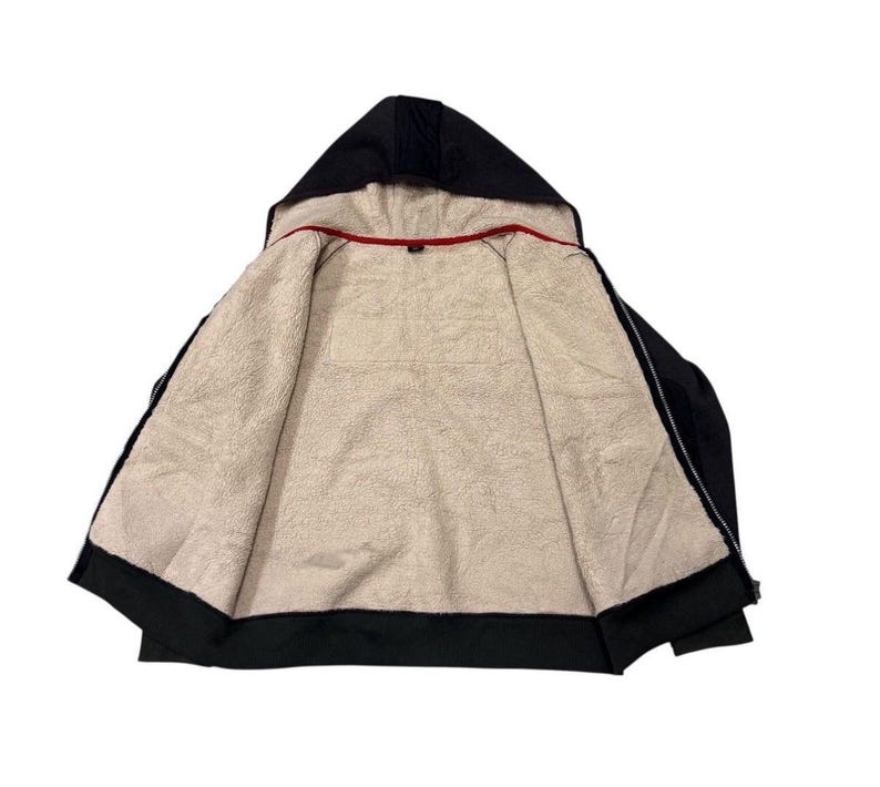 May include: Black hooded zip-up jacket with a soft, cream-coloured fleece lining. The hood is lined with the same fleece material. A red trim is visible along the inside collar. The jacket is open, displaying the interior.
