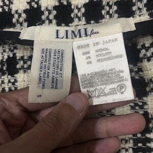 May include: Close-up of a black and white woven fabric with a tag that reads "LIMI feu" and "MADE IN JAPAN." The tag lists the fabric composition as 95% wool, 3% nylon, and 2% polyurethane. Washing instructions are also included.