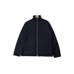 May include: A navy blue quilted jacket with a brown collar and trim. The jacket has a full-length zipper and two front pockets. It is hanging on a wooden hanger.