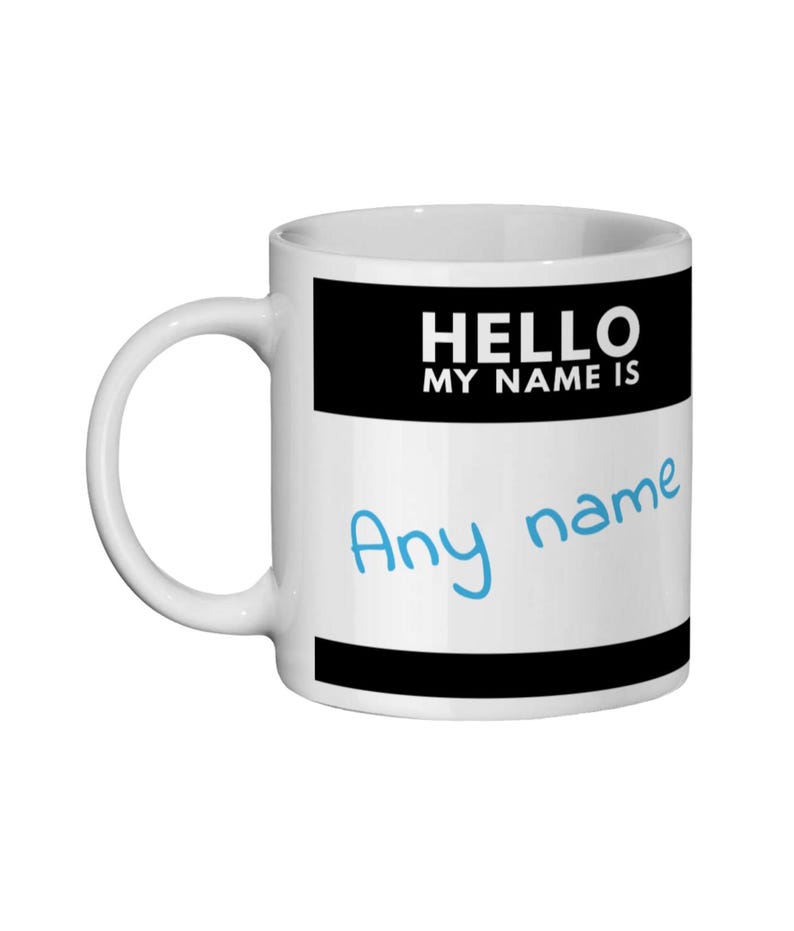 Pu&ograve; includere: Tazza in ceramica bianca con una fascia nera nella parte superiore e inferiore. La tazza ha il testo "HELLO MY NAME IS" in bianco su sfondo nero. Sotto, in scrittura blu, il testo "Any name".