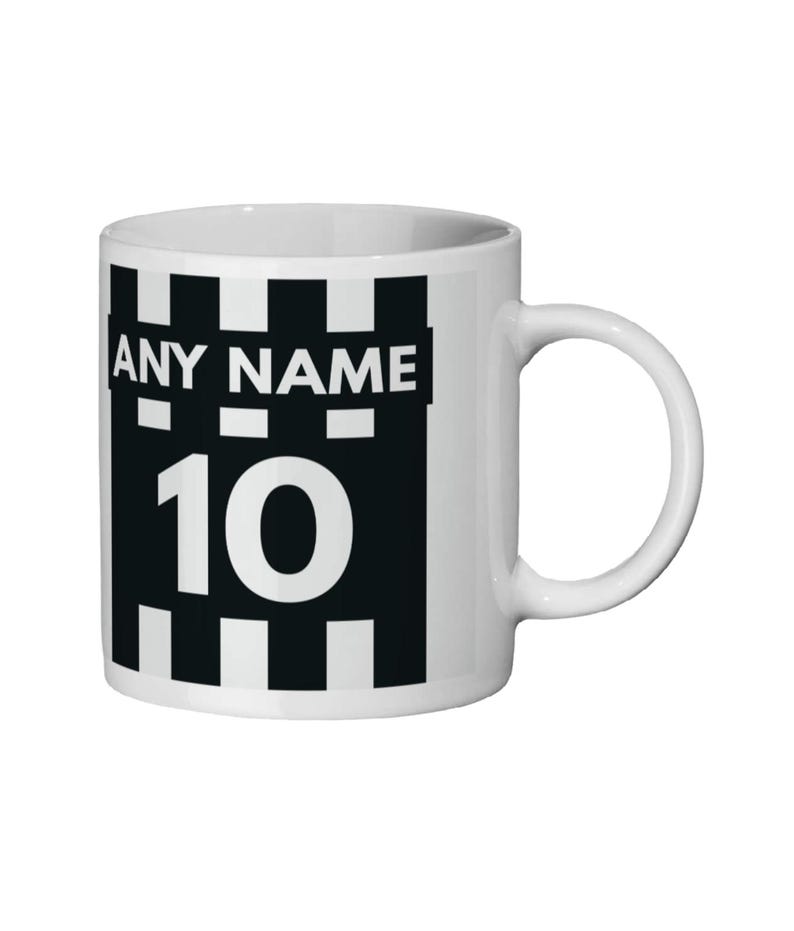 May include: White ceramic mug with a black and white design. The design includes the text "ANY NAME" above the number "10". The mug has a curved handle and a cylindrical shape. The design is reminiscent of a sports jersey.