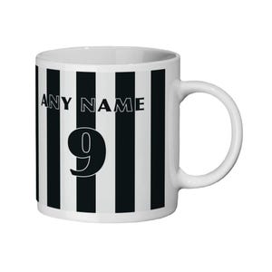May include: White ceramic mug with black vertical stripes. The mug features the text "ANY NAME" above the number "9" in a bold, black font. The mug has a white handle and a simple, clean design.