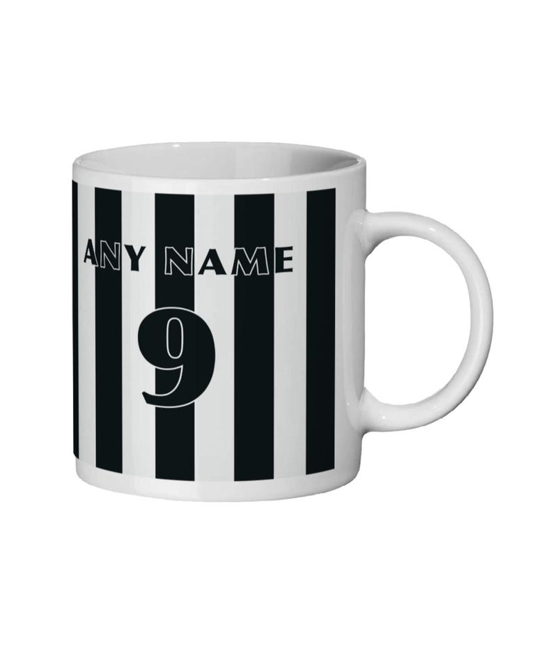 May include: White ceramic mug with black vertical stripes. The mug features the text "ANY NAME" above the number "9" in a bold, black font. The mug has a white handle and a simple, clean design.