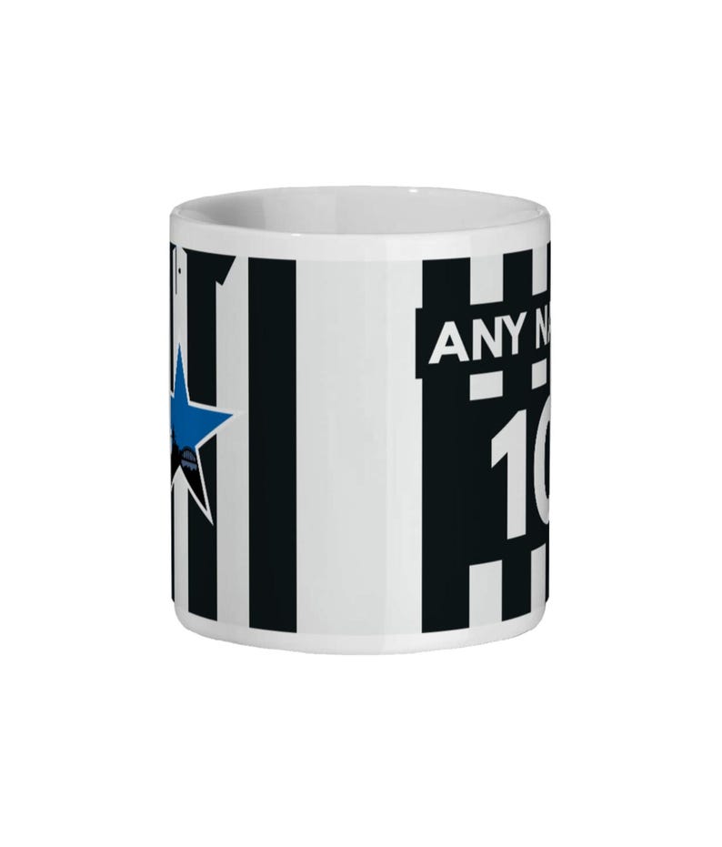 May include: White ceramic mug with black vertical stripes and a blue star design. The mug features the text "ANY N" and the number "10". The mug is cylindrical and has a white interior.