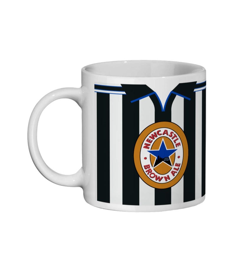 May include: White ceramic mug with a black and white striped design, resembling a football shirt. The mug displays a circular emblem with a blue star and the words "Newcastle Brown Ale".