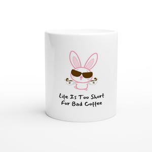 Può includere: Tazza da caffè in ceramica bianca con un coniglietto dei cartoni animati con occhiali da sole e tazze da caffè. La tazza ha il testo "Life Is Too Short For Bad Coffee" in nero.