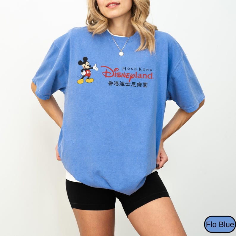 Op de afbeelding: Een blauw T-shirt met korte mouwen met de tekst "Hong Kong Disneyland" in rood en zwart. Het shirt heeft een afbeelding van Mickey Mouse. Het shirt heeft een effen blauwe kleur.