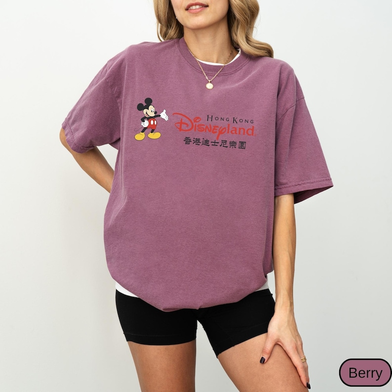 Op de afbeelding: Bessenkleurig T-shirt met Mickey Mouse en het Disneyland Hong Kong logo. Het ontwerp bevat het Disneyland logo in rood en de tekst "Hong Kong Disneyland" in het Engels en Chinees. Het shirt heeft korte mouwen en een ronde hals.