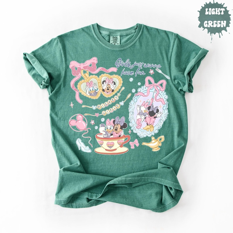 Może przedstawiać: Jasnozielony t-shirt z kr&oacute;tkim rękawem z nadrukiem graficznym przedstawiającym postacie Disneya: Daisy Duck i Minnie Mouse. Wz&oacute;r zawiera tekst Girls just wanna have fun oraz Disney Girls, a także ilustracje medalionu, lustra, filiżanki i lampy.