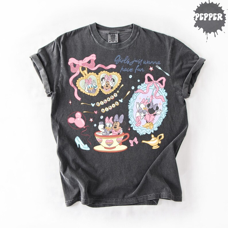 Może przedstawiać: Ciemnoszary t-shirt z nadrukiem graficznym zawierającym tekst "Girls just wanna have fun" oraz "DISNEY GIRLS". Wz&oacute;r zawiera ilustracje Myszki Minnie i Kaczki Daisy, medalion w kształcie serca, filiżankę, lustro oraz złotą lampę.