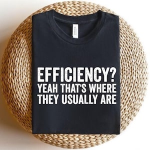 May include: A black short-sleeved t-shirt featuring white distressed text that reads EFFICIENCY? YEAH THAT'S WHERE THEY USUALLY ARE. The shirt has a crew neckline and a visible brand label at the inner collar, presented in a folded, flat-lay style.