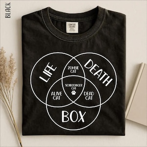 Peut inclure: Un t-shirt noir avec un diagramme de Venn blanc imprimé. Le texte Life, Death, Box entoure les sections contenant Zombie Cat, Alive Cat, Dead Cat et Schrodinger Cat, avec une petite icône de patte au centre du motif graphique.