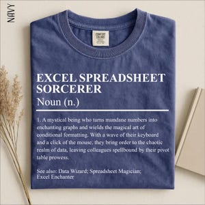May include: A navy blue crew neck t-shirt featuring white text that reads: EXCEL SPREADSHEET SORCERER Noun (n.) 1. A mystical being who turns mundane numbers into enchanting graphs and wields the magical art of conditional formatting. See also: Data Wizard.