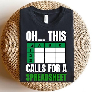 May include: Black t-shirt with the text "OH... THIS CALLS FOR A SPREADSHEET" in white and green. The design includes a spreadsheet grid with letters and numbers. The shirt is displayed on a woven surface.