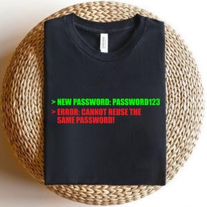 May include: Black t-shirt with the text "NEW PASSWORD: PASSWORD123" in green and "ERROR: CANNOT REUSE THE SAME PASSWORD!" in red. The shirt is displayed on a woven, circular surface.