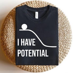 May include: Black t-shirt with the white text "I HAVE POTENTIAL" and a graphic of a white ball on a curved line. The shirt is displayed on a woven, circular surface.