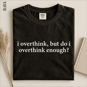 Pode incluir: Uma t-shirt preta de manga curta com decote redondo. O centro da t-shirt apresenta o texto branco "i overthink, but do i overthink enough?" numa fonte serifada. A etiqueta interior do pescoço diz "Comfort Colors".