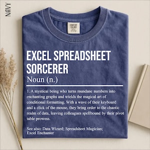May include: A navy blue crew neck t-shirt featuring white text that reads: EXCEL SPREADSHEET SORCERER Noun (n.) 1. A mystical being who turns mundane numbers into enchanting graphs and wields the magical art of conditional formatting. See also: Data Wizard.