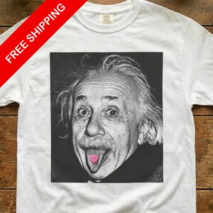 May include: White t-shirt featuring a black and white image of Albert Einstein sticking out his tongue, with a pink tongue. The shirt has a crew neck and short sleeves. The text "FREE SHIPPING" is on the top left.