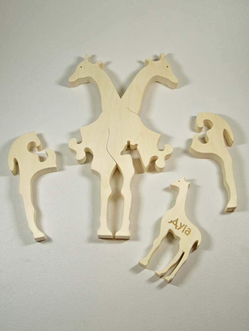 Op de afbeelding: Houten puzzel met vijf stukken die samen een giraffe vormen. De giraffe heeft de naam "Ayla" gegraveerd op zijn lichaam.