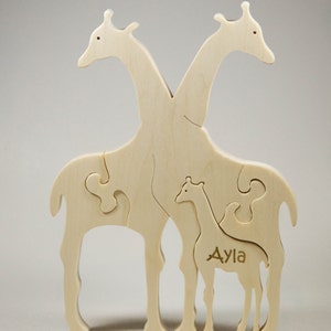 Op de afbeelding: Houten puzzel van een giraffenfamilie, met twee volwassen giraffen en een babygiraf. De babygiraf is gelabeld met "Ayla".