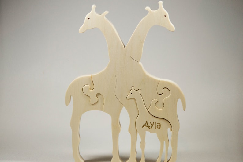 Op de afbeelding: Houten puzzel van een giraffenfamilie, met twee volwassen giraffen en een babygiraf. De babygiraf is gelabeld met "Ayla".