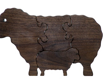 May include: A wooden puzzle of a sheep and a lamb, made from dark brown walnut wood. The puzzle is made of three pieces that fit together to form the complete image.