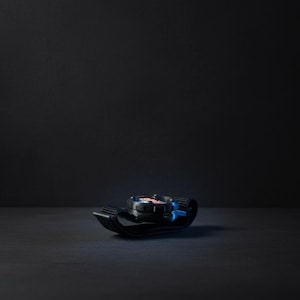 May include: A black and blue watch with a black strap. The watch face has red, white, and blue accents. The watch is lying on a dark surface.