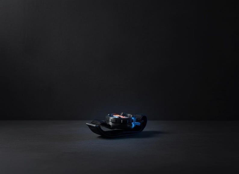 May include: A black and blue watch with a black strap. The watch face has red, white, and blue accents. The watch is lying on a dark surface.