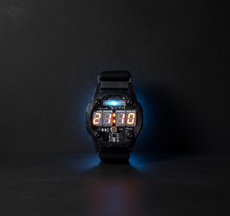 May include: Black digital wristwatch with a futuristic design. The watch face displays the time in orange digital numbers. The watch has a black strap and a blue light emanating from the face.