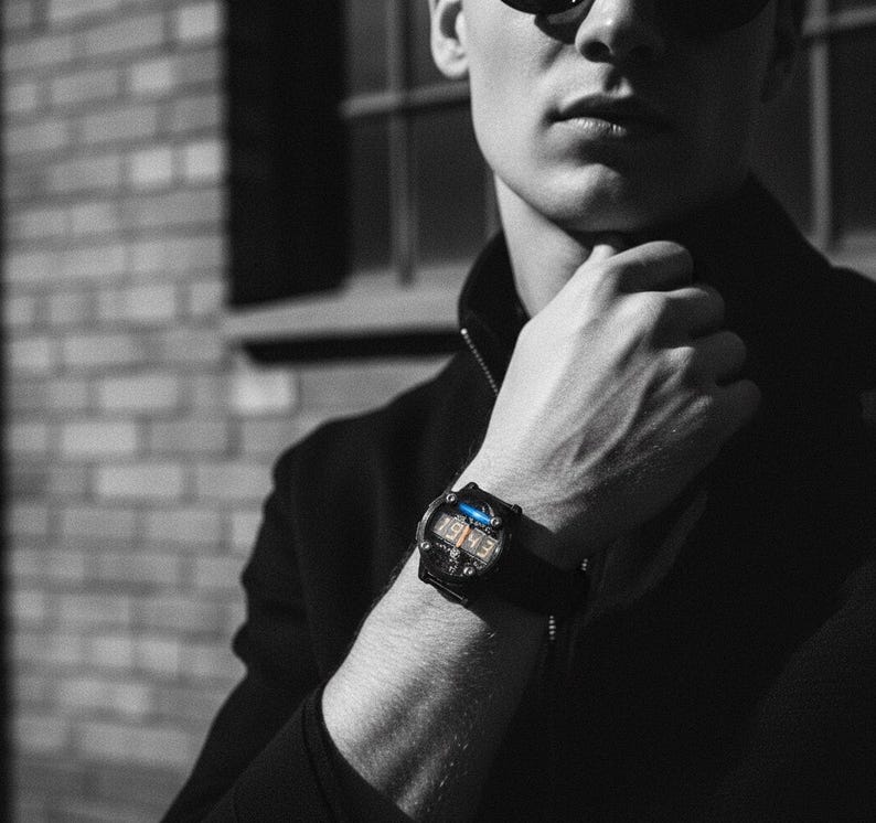 May include: Black digital watch with a rectangular face and a black strap. The watch displays the numbers "1943" in a digital format. The watch is worn on a wrist, with a dark background.