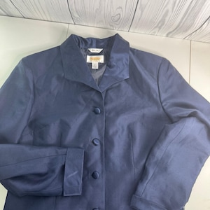May include: A navy blue button-down blazer with a notched collar. The blazer has long sleeves with buttoned cuffs and a tailored fit. The garment has a satin-like sheen and a classic design, suitable for professional or formal wear.