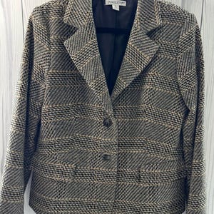 Pode incluir: Blazer Pendleton com um padrão xadrez clássico. O casaco apresenta um forro preto e dois botões. A paleta de cores inclui preto, bege e cinza. O blazer está pendurado num cabide preto.