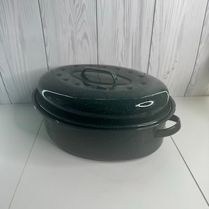 Könnte beinhalten: Ein ovaler, dunkelgrüner Bräter mit gesprenkelter Emaille-Beschichtung. Der Bräter verfügt über einen passenden Deckel mit einem mittigen Griff sowie zwei seitliche Griffe an der Basis. Die Oberfläche glänzt und das Design ist tief und geräumig.