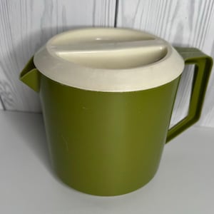 May include: A green plastic pitcher with a white lid. The pitcher has a handle and a spout for pouring. The lid has a recessed area for easy opening. The pitcher is likely used for serving beverages.