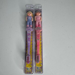 May include: Two children's toothbrushes featuring Cabbage Patch Kids dolls. One is purple with a floral design, the other is pink with a strawberry. Both have soft bristles and are in their original packaging.